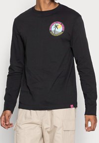 Schwarzes Langarmshirt aus Baumwolle mit grafischem Rundmotiv eines Palmenbaums und einer Sonne sowie dem Text "SUMMERTIME OASIS." Pinker Logosticker am Saum.
