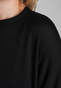 Schwarzer Strickpullover mit einem gerippten Rundhalsausschnitt und einer weichen, strukturierten Oberfläche. Der Stoff scheint leicht und atmungsaktiv zu sein.