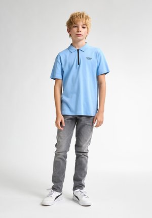Světle modré polo tričko s krátkým rukávem a zipovým límcem, spárované se slim-fit šedými džíny a bílými sportovními botami.
