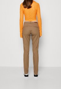 Beżowe dopasowane spodnie o gładkiej fakturze, z dwoma tylnymi kieszeniami. Do tego jasnopomarańczowa, teksturowana bluzka z długim rękawem.