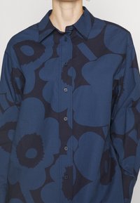 Chemise à boutons bleu marine avec de grands motifs floraux bleu foncé, col à pointes écartées et texture de tissu lisse.