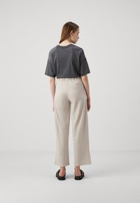 T-shirt gris coupe courte à manches courtes, associé à un pantalon large beige avec une taille élastique. Des sandales noires complètent la tenue.