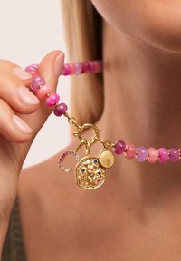 Kolorowa naszyjnik z koralików z okrągłymi różowymi i fioletowymi koralikami, z złotym zawieszką z wzorem lwa i kolorowymi kamieniami szlachetnymi.
