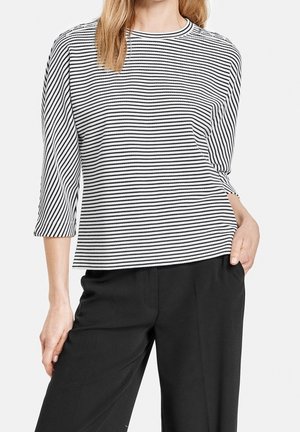 Black and white striped long-sleeve top with a rounded neckline and relaxed fit, paired with black, loose-fitting trousers.