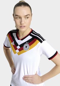 White soccer jersey featuring a v-neck, black and red stripes on sleeves, and a diagonal pattern in red, yellow, and black. German Football logo displayed.