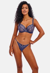 Marineblauwe lingerie set met een doorzichtige mesh beha met kantdetails en een bijpassende thong. Beide hebben subtiele accenten en fijne stiksels.