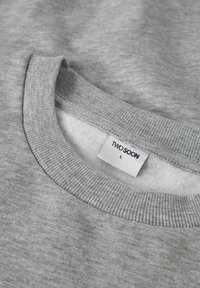 Felpa grigia con scollo a costine e interno morbido. Presenta un'etichetta con la scritta "TWO SOON" e la taglia "L". Tessuto liscio e strutturato.