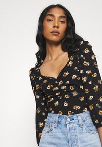 Sort blomstret top med firkantet halsudskæring, lange ærmer og samlet detalje. Kombineret med højtaljede lyse denimshorts.