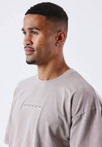 Camiseta gris claro de manga corta, con un parche texturizado del logo "PXP" en la parte delantera, corte relajado y fabricada en algodón suave.