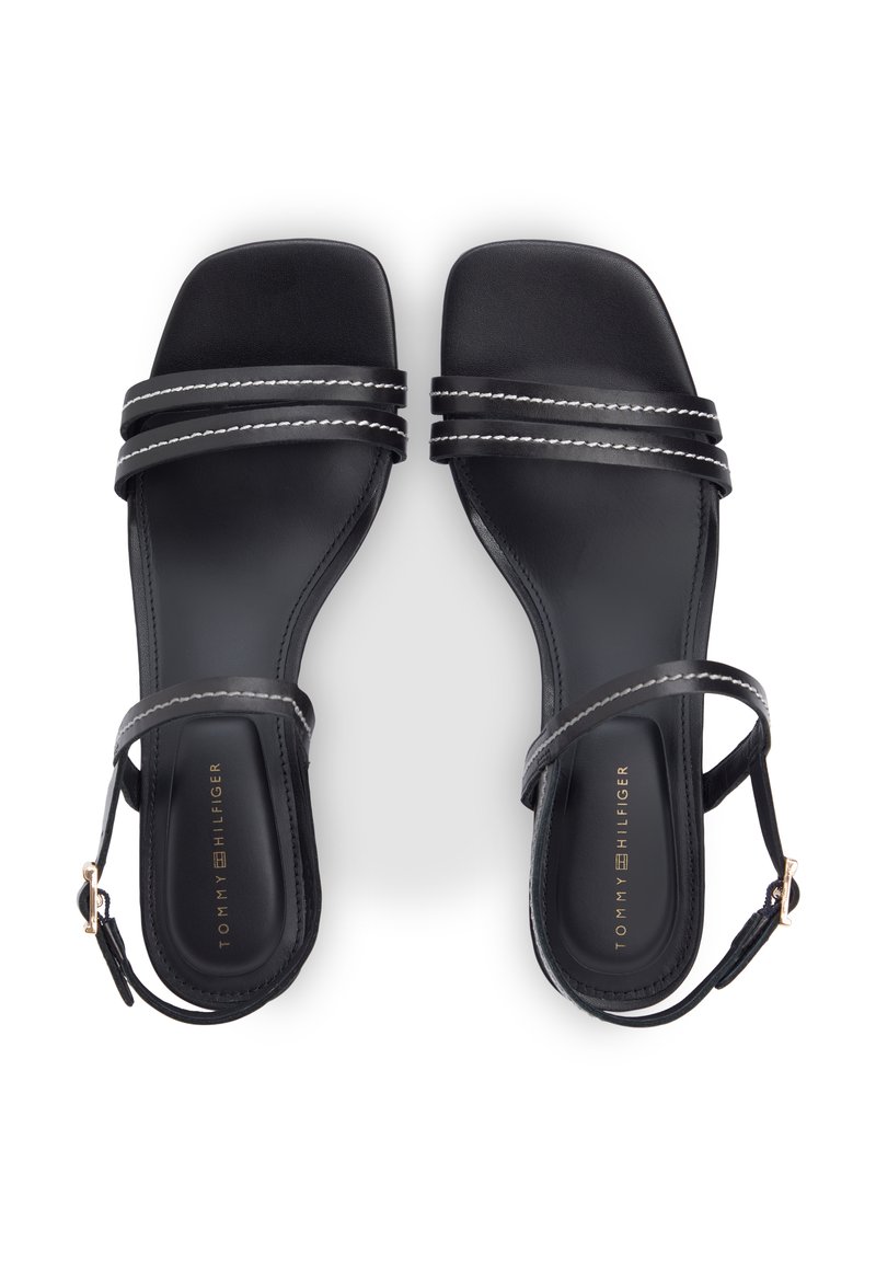 Sandalias planas negras con correas de doble costura y hebillas en el tobillo, con la marca "Tommy Hilfiger" en las plantillas.