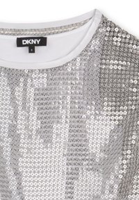 Haut couvert de sequins argentés avec encolure ronde blanche et étiquette noire DKNY taille 8 à l'intérieur du col.