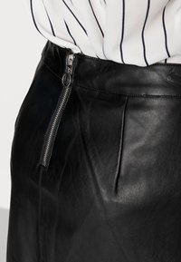 Gonna di pelle nera con zip laterale in metallo argentato, texture liscia e dettagli di cucitura in vista. Abbinata a una blusa bianca a righe.