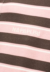 Κοντινή λήψη ροζ και καφέ υφάσματος με οριζόντιες ρίγες και λευκό κεντητό κείμενο "NAPAPIJRI".