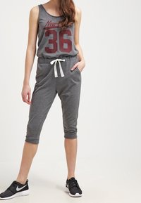 Completo sportivo grigio con top senza maniche, stampato con "New York 36", vita sagomata e pantaloni corti. Coulisse bianca e texture morbida.
