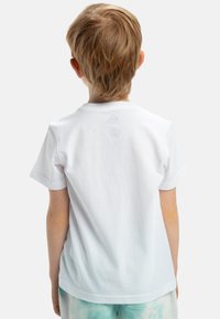 Camiseta de algodón blanca con mangas cortas, cuello redondo y textura suave. Presenta un pequeño detalle de logo en el cuello de la parte trasera.