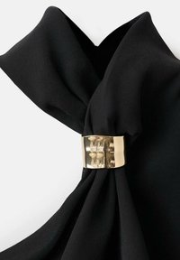 Cortinas de tela negra con un broche metálico dorado que presenta un patrón texturizado, asegurando el material en un diseño plegado.