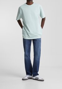 T-shirt en coton vert menthe clair à manches courtes, associé à un jean en denim droit bleu marine et des baskets gris-blanc avec des rayures noires.