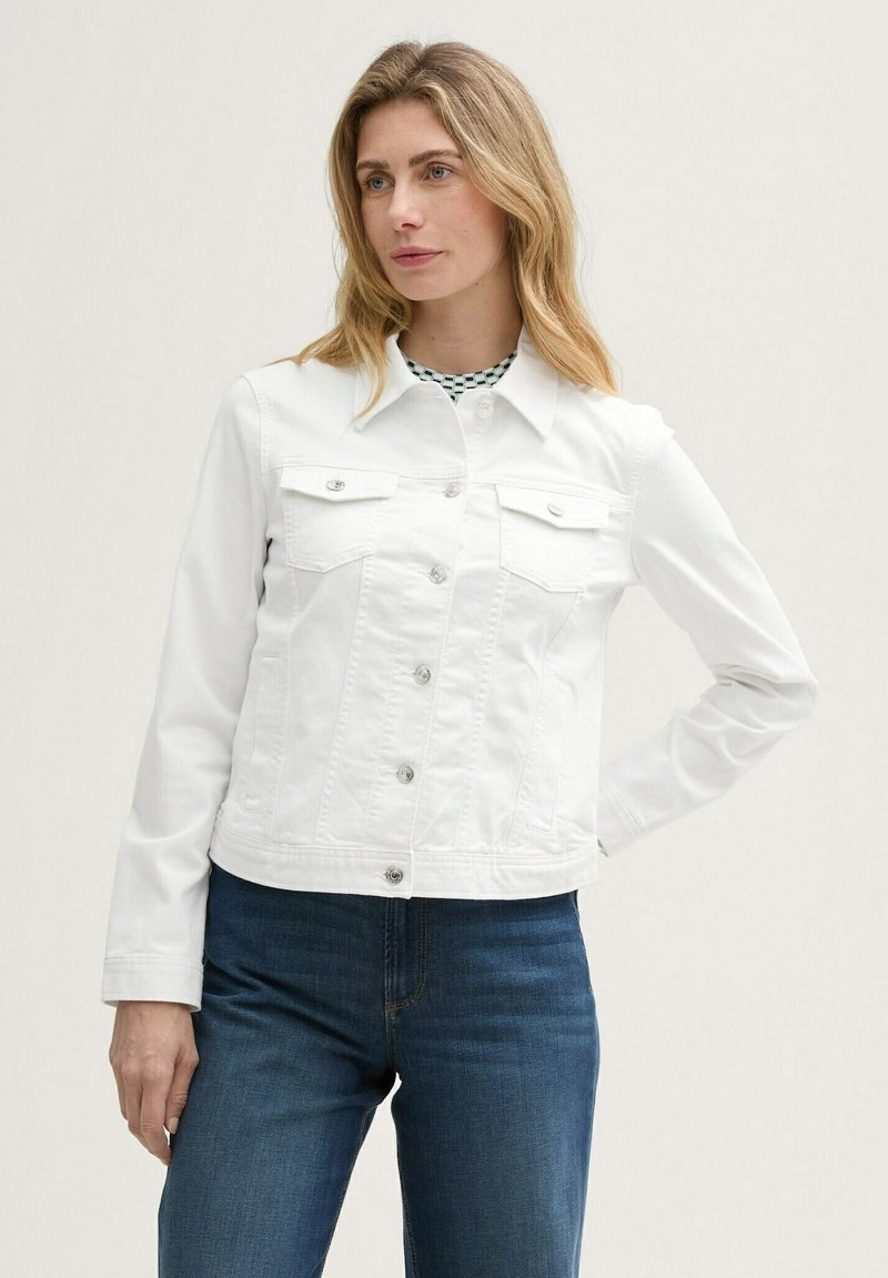 Veste en denim blanc avec un col, fermeture à boutons et deux poches poitrine. Manches longues et design ajusté. Portée sur un top à carreaux verts.