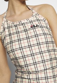 Top halter FILA w beżowym materiale w czarno-czerwony wzór w kratę. Posiada logo marki z przodu oraz regulowane ramiączka na szyi.