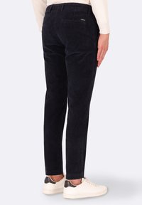 Pantaloni in corduroy blu navy con vestibilità slim, caratterizzati da righe verticali, tasca posteriore e un discreto dettaglio del logo. Abbinati a sneakers bianche.