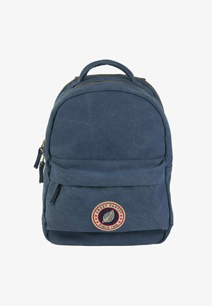 Sac à dos en toile marine avec un dessus arrondi, zips dorés, poche avant et un patch logo circulaire représentant une feuille, avec des accents rouges et blancs.