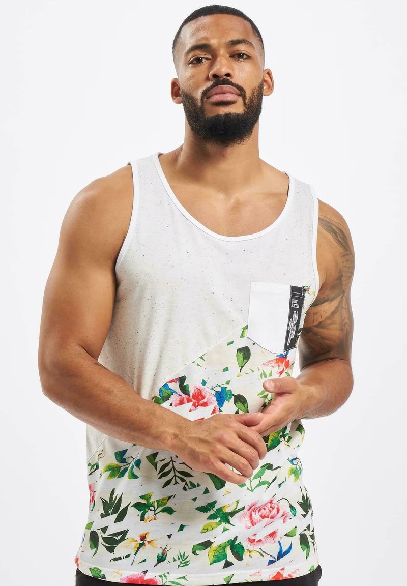 Hvid tanktop med blomsterprint i pink, grøn og gul. Har en frontlomme med sort-hvide detaljer. Materialet er bomuld.