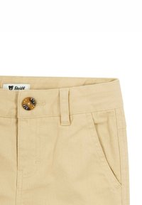 Beige Baumwollhosen mit einem Knopfverschluss und einem Logo. Zwei Fronttaschen und Gürtelschlaufen, mit sichtbaren Nähdetails.