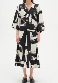 Pitkä musta-valkoinen mekko, jossa on abstrakti siveltimen vedon kuvio, V-pääntie ja leveät hihat; kevyt materiaali, joka laskeutuu kauniisti.