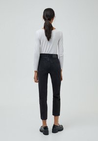 Jeans de mezclilla negra con corte recto, talle medio y bolsillos traseros visibles. Combinados con una blusa blanca de manga larga y zapatos negros.