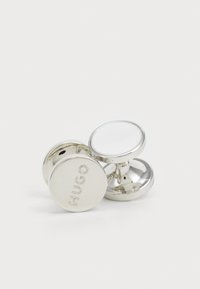 Silver cufflinks med en polerad yta, som har en cirkulär form och det ingraverade varumärket "HUGO" på ena sidan.