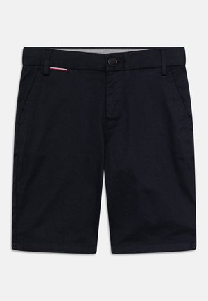 Shorts bleu marine en tissu lisse. Ils comportent deux poches latérales, une fermeture frontale par bouton, et un petit accent rouge et blanc sur la ceinture.