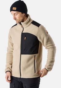 Beige fleece jacket with black panels, high collar, zippered front pocket, and leather accents. Textured fabric and fitted design.