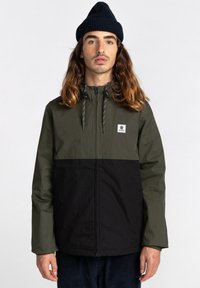 Grüne und schwarze Zip-Jacke mit Kapuze, ausgestattet mit Zugbändern, langen Ärmeln und einem rechteckigen Logo-Patch auf der Brust.