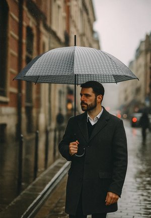 Black and gray checked umbrella held by a man in a dark coat, standing on a wet street with blurred city lights in the background.