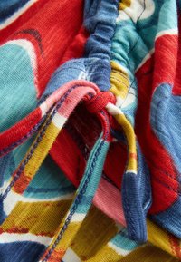 Tela colorida con una mezcla de patrones en rojo, azul, verde azulado, amarillo y rosa. Presenta detalles de elástico fruncido y costuras en contraste.