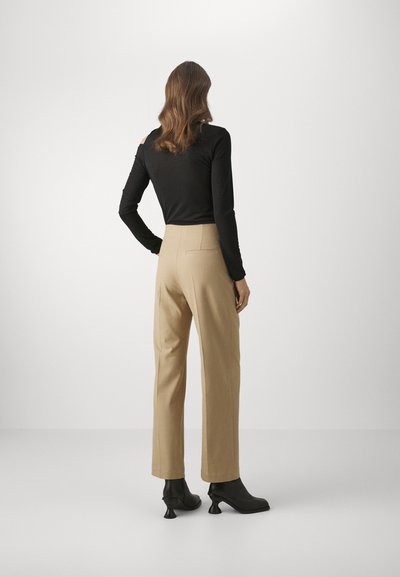 Zwarte langekous top met open schouders, gecombineerd met beige high-waisted broeken en zwarte haklaarzen. Glad materiaal en gepaste pasvorm.