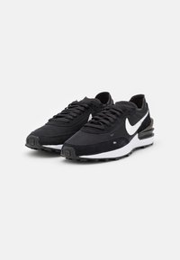 Fekete sportcipők hálós felső résszel, velúr díszítésekkel, fehér Nike logóval, párnázott bokával és textúrázott gumitalppal.
