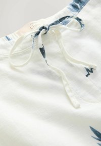 Hørshorts i hvid med en dekorativ blå kant ved taljen og et matchende bindebånd. Har et let, tekstureret stof.