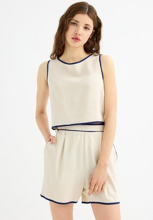Top sin mangas beige y pantalones cortos a juego con ribetes en azul marino. La tela parece ligera y ligeramente texturizada, con un corte relajado.