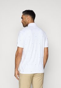 Λευκό πόλο μπλουζάκι με ανοιχτό μπλε γεωμετρικά σχέδια, κοντά μανίκια και γιακά. Λείο υφάσμα και προσαρμοσμένη εφαρμογή.