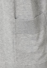 Suéter de punto gris claro con un bolsillo y dobladillo acanalados. La textura es suave con un sutil patrón de fibras blandas entrelazadas.