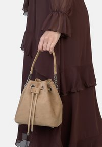 Borsa a secchiello in camoscio beige con chiusura a coulisse e occhielli in tinta argento; presenta un manico corto abbinato a un dettaglio a catena.