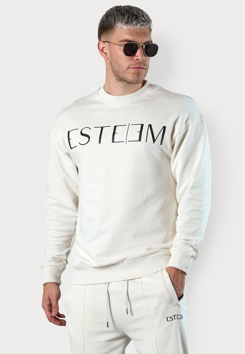 Light cream sweatshirt with black "ESTEEM" logo across the chest. Features ribbed cuffs and hem, paired with matching sweatpants.