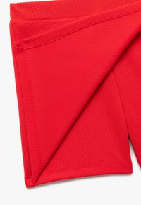 Røde atletiske shorts lavet af struktureret stof med en glat talje og flade sømme, der har et foldet design til visning.