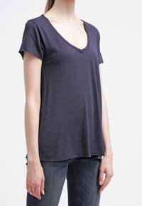 Námořnická modrá tričko s výstřihem do "V" vyrobené z lehké tkaniny, s krátkými rukávy a volným střihem, má jemnou strukturu a boční rozparky.