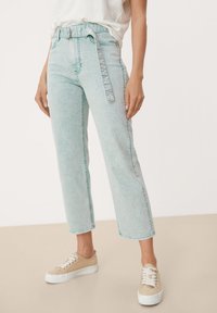 Jeans de denim azul claro con cintura alta, pierna ancha y cinturón extraíble. Presentan costuras en contraste y una textura ligeramente descolorida.