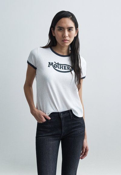 T-shirt blanc avec un graphisme noir "MOTHER", doté d'un col rond et de bordures bleu foncé, associé à un jean en denim foncé.