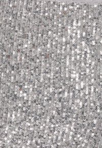 Krupni plan gusto složenih srebrnih sjaja na tkanini koja reflektira svjetlost s blistavim, sjajnim učinkom.