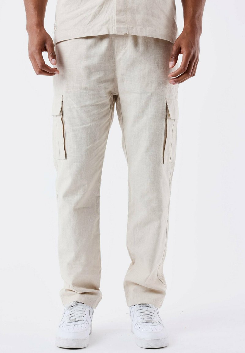 Beige cargo bukser lavet af tekstureret stof, med sidelommer og en afslappet pasform, parret med hvide sneakers.