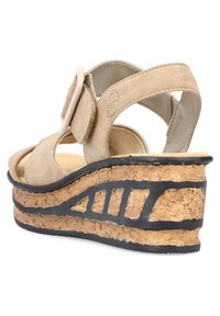 Sandalo in camoscio beige con fibbia regolabile, dotato di una suola a cuneo in sughero e una suola in gomma nera testurizzata con motivi intagliati.